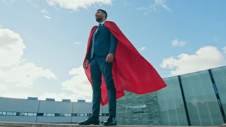Businessman Superhero WIth Red Cape Blowing in the Wind Stands on the Roof of a Skyscraper Ready to Make Business Transactions and Save the Day. Low Angle Shot.
