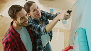 Young Beautiful Couple Decorate Their New Apartment. Husband and Wife are Painting the Wall with Rollers that are Dipped in Light Blue Paint. They Hug. Renovations at Home.