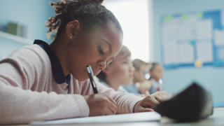 In Elementary School Classroom Black Girl Writes in Exercise Notebook