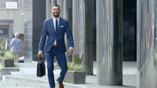 Smiling Business Man with a Bag Walks in a Business District. Weather Is Sunny He Looks Handsome in His Tailored Suit.