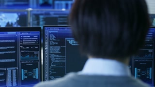 In the System Control Room Technical Operator Stands and Monitors Various Activities Showing on Multiple Displays with Graphics. Administrator Monitors Work of  Artificial Intelligence, Big Data Mining, Neural Network, Surveillance Project.