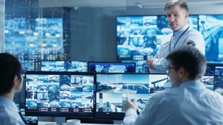 In the Security Control Room Chief Surveillance Officer Holds a Briefing for Two of His Subordinates. Multiple Screens Show that They Guard Object of International Importance.