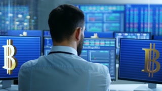 Stock Exchange Trader Works With Cryptocurrency at His Workstation. Screens Show Ticker Numbers and Graphs.
