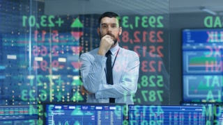 Stock Market Top Trader Looks at Projected Ticker Numbers and Graphs Running, Analysing Data to Make Best Sell. Behind Him Room Full of Screens and Statistics.