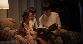 Portrait of Two Active Children Engaged in a Conversation with their Father While He Reads to them Before Bed. Cute Korean Kids not Ready to Go to Sleep, Reading a Story With their Male Parent