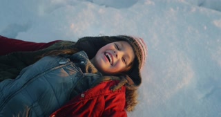 Cinematic shot of carefree happy smiling little girl having fun to lying on snow and enjoy to spen