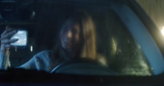 Woman Sitting in a Car Using Smartphone on a Rainy Night