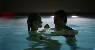 An young couple is embracing and having relax in an outdoor illuminated with night lights swimmin
