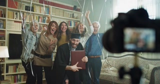 A Diverse Group, Including an Elderly Man, Celebrates a Graduation With Balloons and Streamers in a Cozy, Book-filled Room, Capturing a Joyful Moment of Unity and Pride in an Lgbt-themed Setting.
