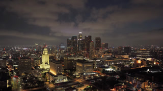 Nighttime panorama of Los Angeles downtown showing City Hall and illuminated skyscrapers with urban neighborhood and busy streets full of