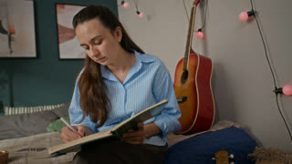 Caucasian young woman sitting on bed, writing in notebook with pen. Footage is perfect for online education promos, student lifestyle campaigns, or creative writing advertisements
