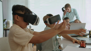 Handheld shot of two boys playing online video game in VR glasses during group IT class