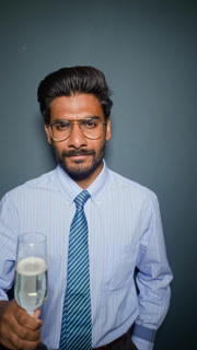Portrait of young adult Indian businessman raising champagne flute to toast. Clip suits corporate holiday celebration ads and new year greetings, vertical