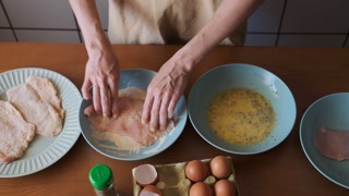 Adult woman breading chicken cutlet at home kitchen, overhead view