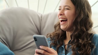 Woman laughing while using mobile phone sitting on luxury chair
