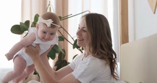 Happy mother playing with her baby girl at home