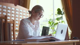Woman using laptop and looking at textbook in library