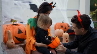 Trick or treat. Little kid wearing halloween costume of skeleton receiving candies at home from his father wearing red glow devil horns