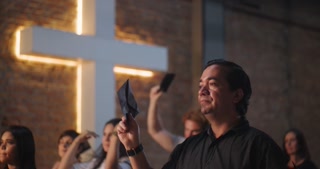 Man of Hispanic descent holding offering envelope inside church, communal gathering, spiritual moment, worship service, focus on individual, group celebration in religious space