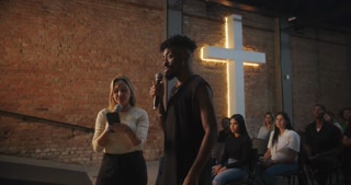 Man and woman singing together during religious ceremony, holding microphones, illuminated cross in background, spiritual energy, engaging performance, diverse participants