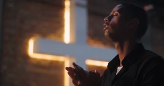 Man with hands lifted in prayer, looking up in faith near illuminated cross, deep spiritual moment of worship, contemplation, and devotion, peaceful reflection on belief