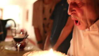 Older man celebrating 70th birthday, senior person blowing birthday candle cake