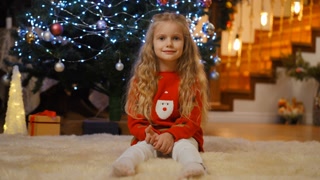 A joyful, happy child sits comfortably on a fluffy rug, right next to a beautifully decorated Christmas tree