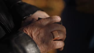A touching close-up of an elderly man's and woman's hands holding a black box with a diamond engagement ring inside. The golden autumn