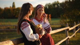 Young woman in embroidered folk blouse closes her eyes and gently inhales the scent of a ripe apple warmed by the sun, standing near a