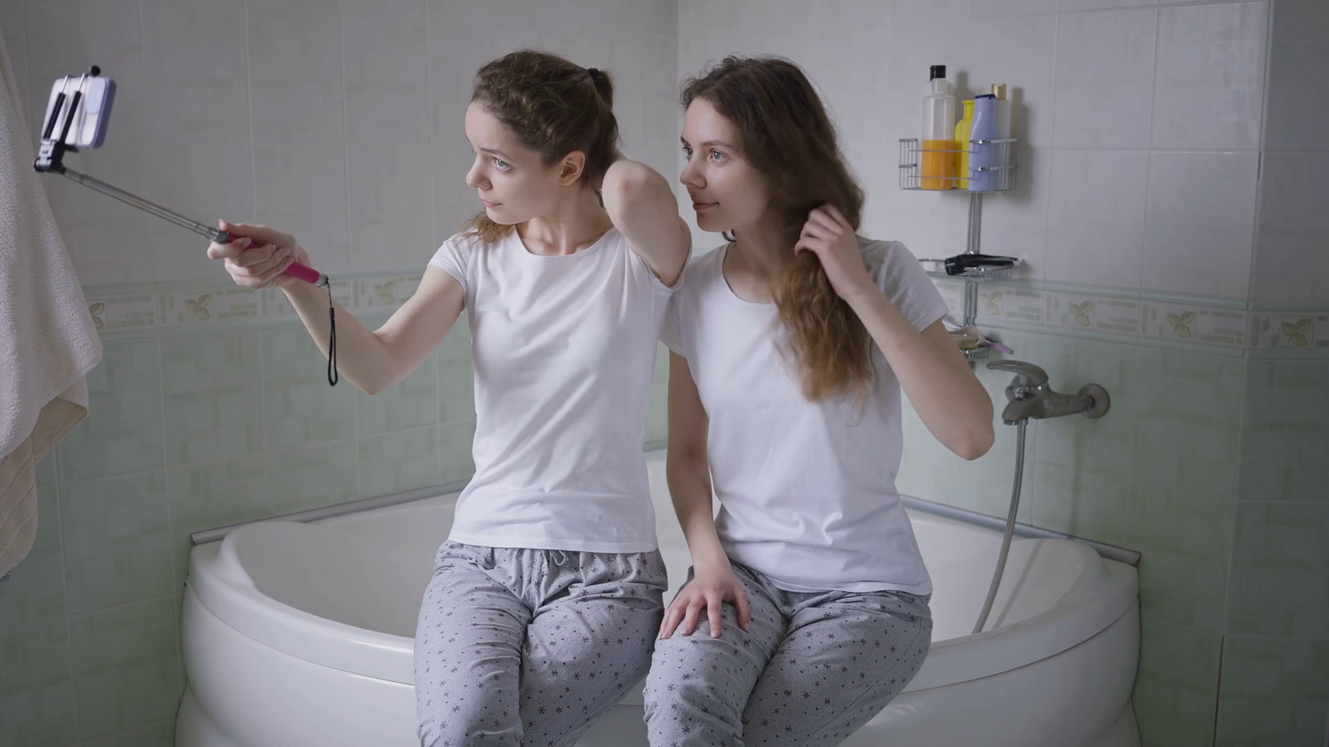 Charming twin sisters sitting on bathtub taking selfie on smartphone