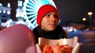 Close-up confident teen boy waiting for a date on Valentine's night in the city. Smiling positive teenager with flowers and balloon. Slow motion.