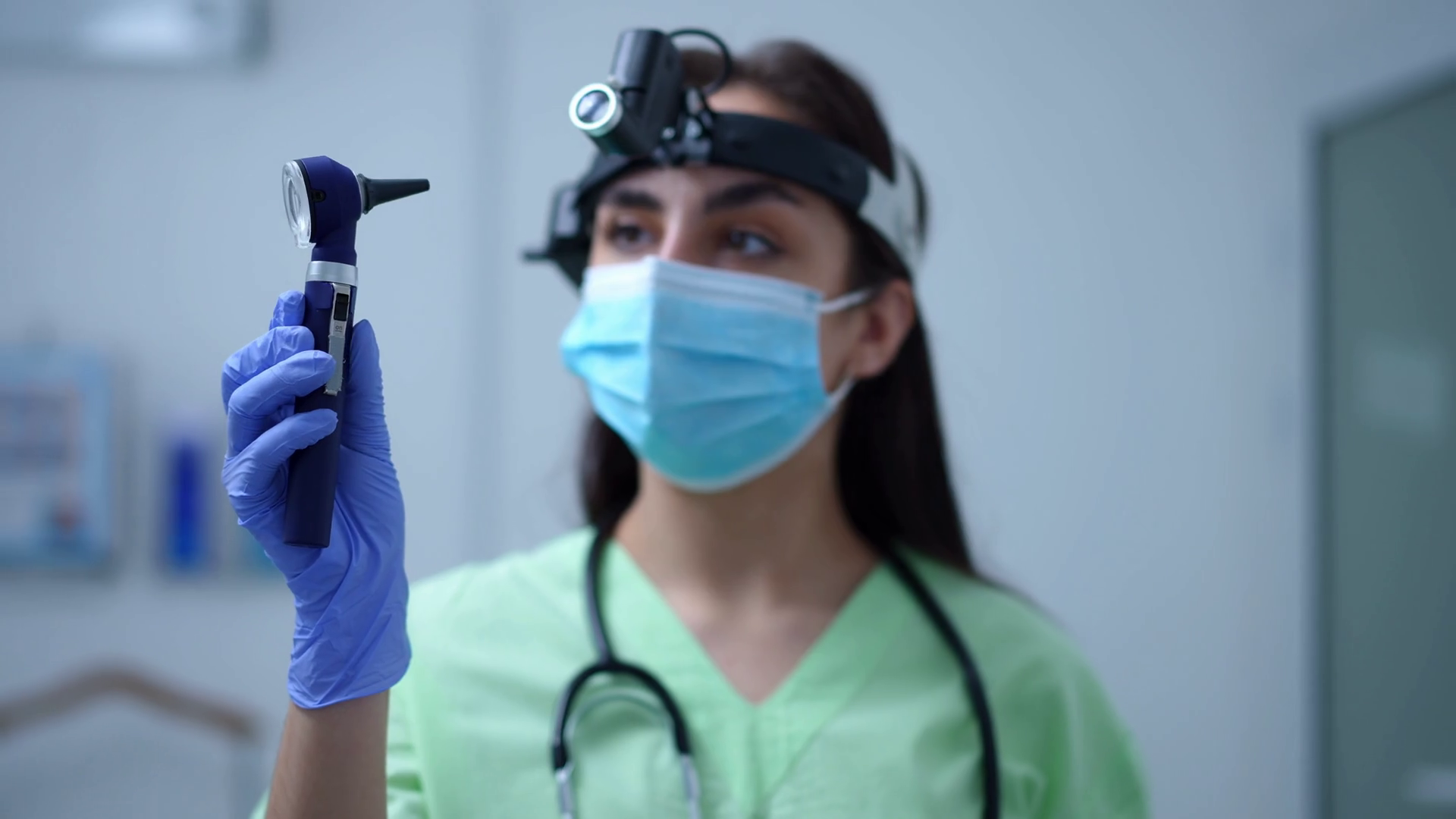 Otoscope in hand of blurred Caucasian female otolaryngologist standing