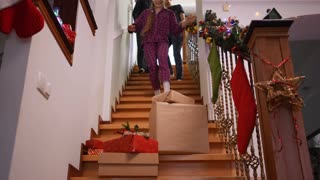 Smiling family walking downstairs to Christmas gifts talking sitting down smiling. Wide shot front view portrait of Caucasian man woman and teenage girl in pajamas rejoicing New Year morning at home.