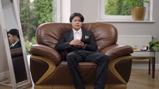 Wide shot of confident Asian thoughtful groom in elegant wedding suit entering living room sitting down on comfortable armchair. Portrait of serious man waiting for marriage ceremony indoors.