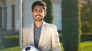 Positive Middle Eastern man juggling soccer ball outdoors. Medium shot portrait of young guy posing with ball on urban street. Sport and hobbies.