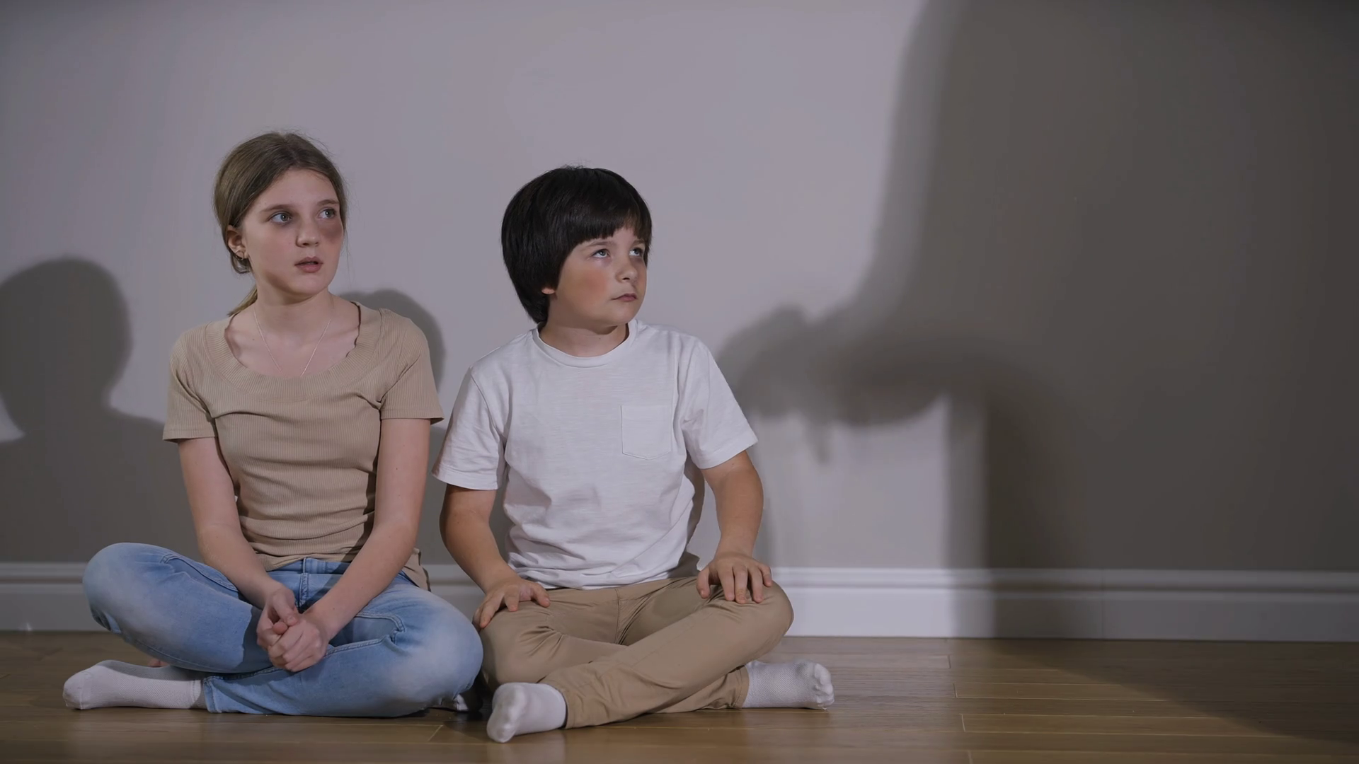 Caucasian brother hugging sister as shadow of violent aggressive parent threatening with belt