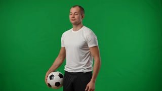 Confident young footballer with soccer ball on green screen
