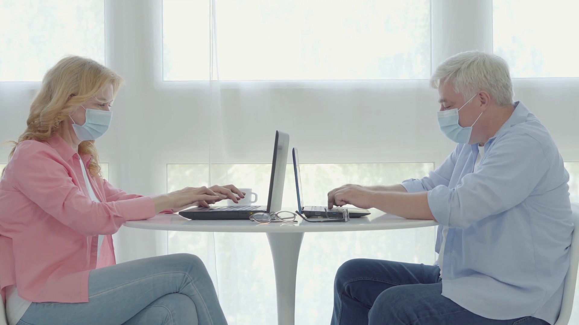 Midadult man and woman in face masks sitting at the table and typing