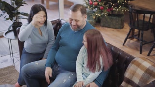Top angle view of positive laughing Caucasian woman and girl giving high-five to cheerful mid-adult man. Portrait of happy Caucasian family enjoying New Year weekends at home. Christmas celebration.
