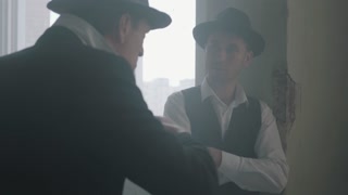 Two stylish men in hats and suits standing in an abandoned building discussing business situation emotionally. The mafia guys have meeting in abandoned building. Cool guys, thugs, mafia, criminal gang