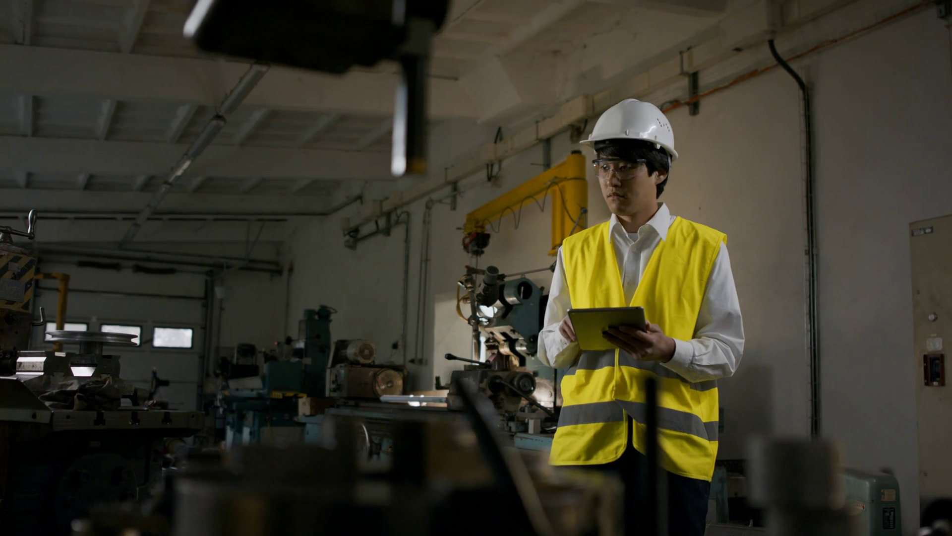 Young industrial Japanese man engineer with protective wear using tablet indoors in metal