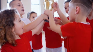 School sports teammates rising up golden trophy after winning sports indoor competition
