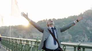 Mature businessman in a city, standing on bridge, stretching arms. Slow motion.