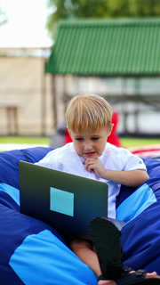 Cute boy sitting outdoor with laptop. Small kid learning outdoor with computer. Vertical video
