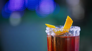 Rotating glass with top decorated with salt and orange peel. Red alcohol cocktail in the bar. Close up. Blurred backdrop.