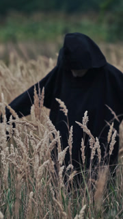 Scary evil figure in nature. Back view on scary ghost in black robe turning with outstretched arms on wheat field. Halloween concept. Vertical video