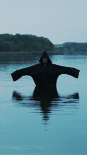 Horror woman soaking in water river. Scary figure in black mantle.. Vertical video