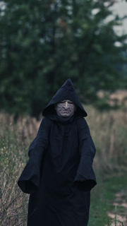 Portrait of scary death in black. Spooky figure in dark mantle with hood coming to camera on nature background. Horror concept. Vertical video