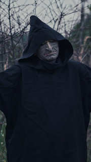 Portrait of terrible ghost outdoors. Scary figure of evil in black costume standing in nature with outstretched arms. Concept of horror. Vertical video