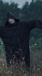 Portrait of ghost with outstretched arms in nature. Scary figure of death in black robe in the field. Horror face of a devil in hood. Vertical video